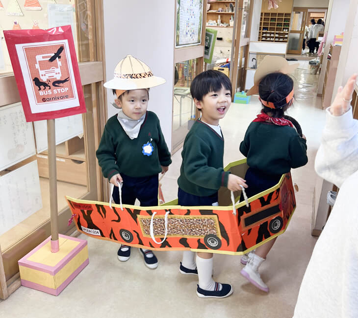 園児が集まってダンボールで作られたバスに乗って遊んでいる