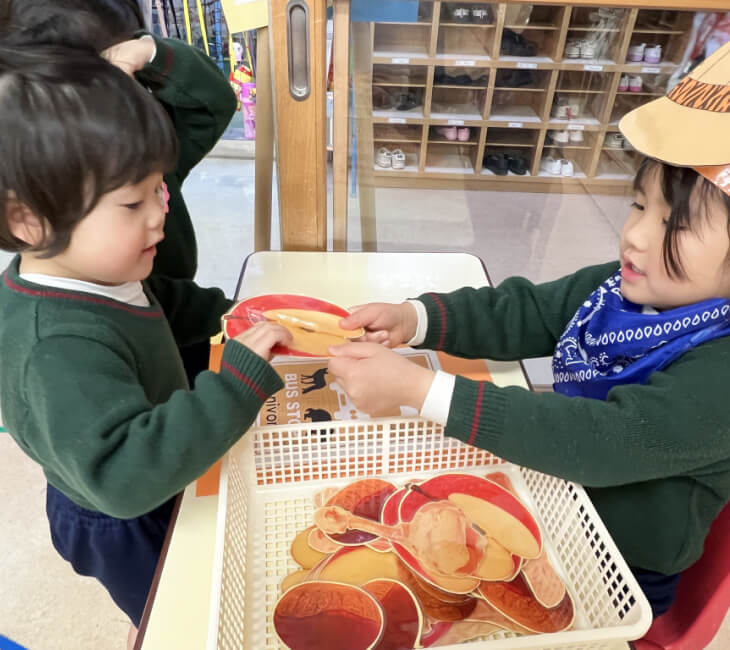 園児がごっこ遊びでおもちゃのリンゴを手渡している