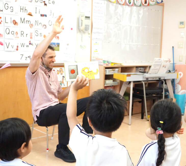 園児たちの英語の授業で先生と生徒が手をあげている
